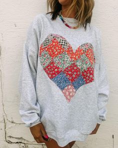 a woman standing in front of a wall wearing a sweatshirt with a heart on it