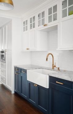 a white kitchen with blue cabinets and gold faucet in the sink, along with wood flooring