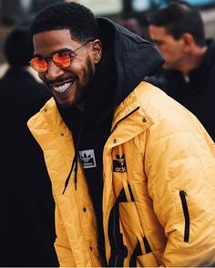 a man in yellow jacket with sunglasses on his face and black hoodie smiling at the camera