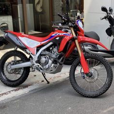 a red motorcycle is parked on the side of the street next to a motocross bike