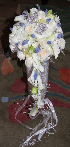 a bouquet of white and blue flowers in a silver vase on the carpeted floor