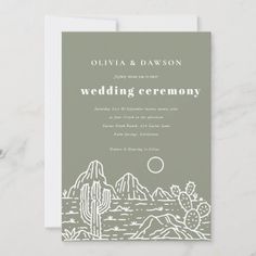 the wedding ceremony card is shown with cactus and mountains in grey, on a marble surface