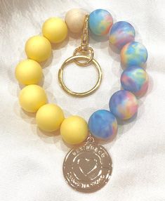 a yellow and blue bracelet with a coin charm on it's end, sitting on a white cloth