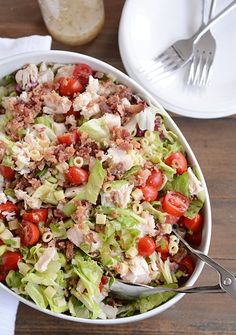 a salad with meat and tomatoes in a white bowl on a wooden table next to silverware