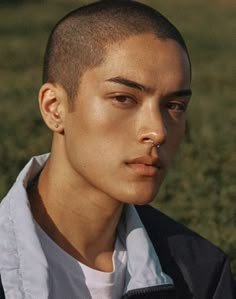 a young man with a shaved head and ear piercings standing in a grassy field