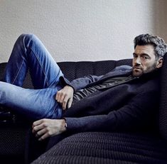 a man laying on top of a couch with his legs crossed and looking off to the side