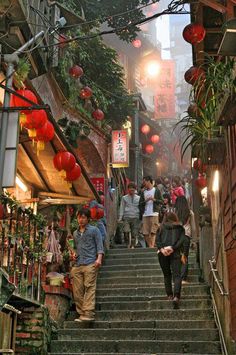 people are walking up and down the stairs in an alleyway with lanterns hanging above them