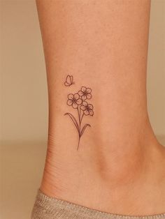 a small flower tattoo on the side of a woman's foot with butterflies flying above it