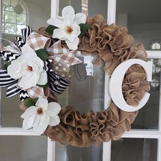 a wreath with white flowers and brown burlocks hanging on the front door window