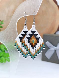 a pair of beaded earrings on top of a wooden table next to a present box