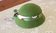 a green hat with a ribbon around the brimmed top on a floral tablecloth