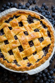 a blueberry pie with latticed crust in a white dish on a wooden table