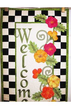 a quilted welcome sign with flowers and leaves on black and white checkered background