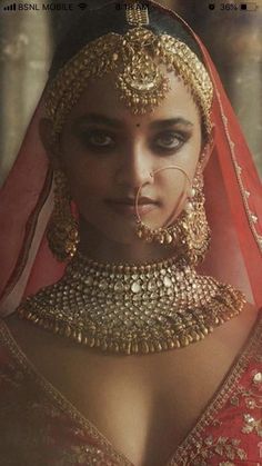 a woman in a red and gold bridal outfit with jewelry on her head, looking at the camera