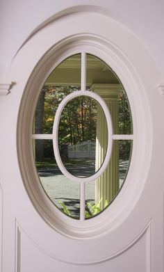 a white door with a circular window in the center and trees behind it, on a sunny day