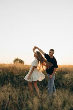 a man and woman dancing in a field at sunset