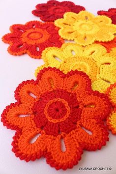 crocheted flowers are arranged in rows on a white tablecloth with orange, yellow and red colors