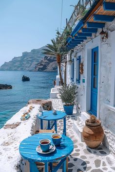 two blue tables sitting on the side of a building next to the ocean with water and mountains in the background