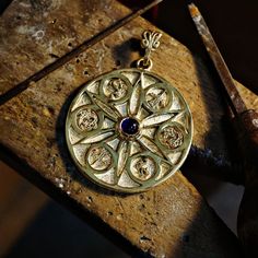 a gold pendant with a blue stone in the center sitting on a piece of wood