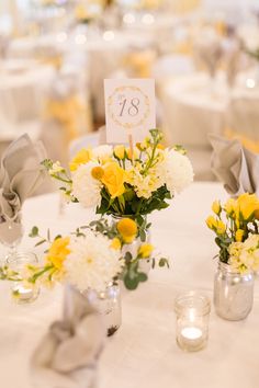 two vases filled with yellow and white flowers sitting on top of a round table