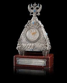 an ornate silver clock sitting on top of a wooden base