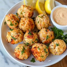 a white plate topped with crab cakes next to lemon wedges and a dipping sauce