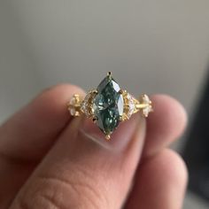 a person holding a ring with a green stone in it's middle and two white diamonds on the side