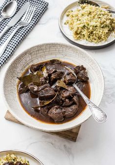 a white bowl filled with beef and brown gravy next to a plate of rice