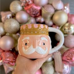 a hand holding a coffee mug with a crown on it's head and ornaments in the background