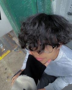 a woman wearing glasses and holding her hand up to her face while sitting on the ground