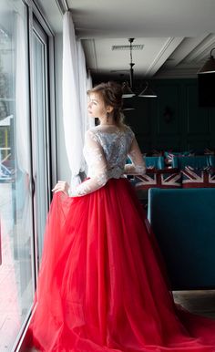 a woman standing in front of a window wearing a long red dress with sheer sleeves