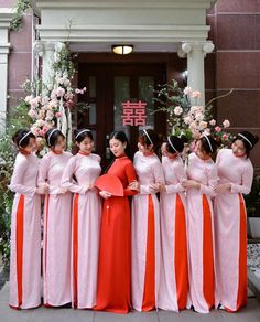 a group of women standing next to each other in front of a building with flowers