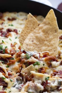 a tortilla chip being dipped with cheese and bacon