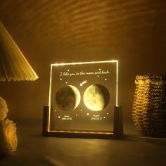 two phases of the moon illuminated in a wooden frame on a table next to a lamp