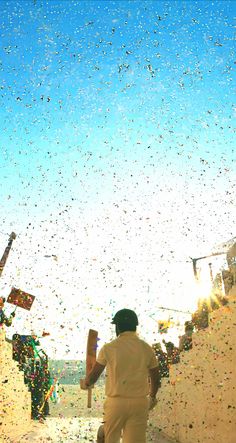 a man holding a baseball bat while walking down a sidewalk covered in confetti