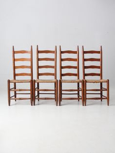 four wooden chairs sitting next to each other on a white floor in front of a wall