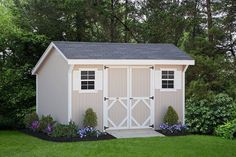 a white shed sitting in the middle of a lush green field