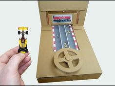 a hand holding a toy car next to a cardboard box with a track in it