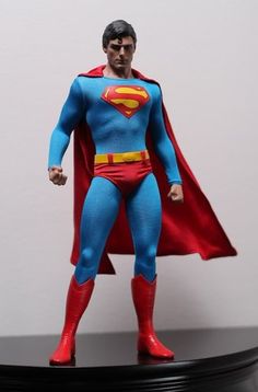 a man in a superman costume standing on top of a black base with a red cape