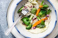 a bowl filled with noodles, broccoli and carrots next to a fork