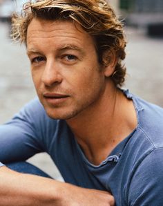 a close up of a person wearing a blue shirt and sitting on the ground with his arms crossed