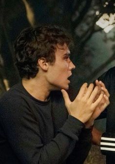 two young men sitting next to each other in front of a tree with their hands together