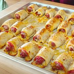 a baking pan filled with hot dogs wrapped in cheese and covered in melted cheese,