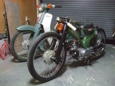 two motorcycles parked next to each other in front of a garage door with tools on the floor