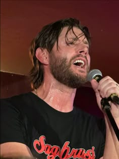 a man singing into a microphone while wearing a black shirt with red lettering on it