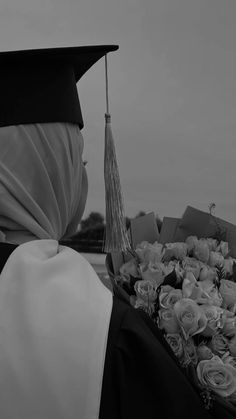 a woman wearing a graduation cap and gown with flowers in front of her, looking at the sky