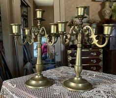 two brass candelabra on a table in a room with other furniture and decor