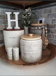 decorative items displayed on wooden tray with brick wall in background, including vase and letter h