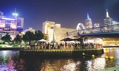 a group of people standing on the side of a river next to a bridge at night