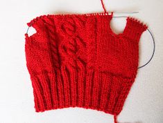 a pair of red knitted mitts sitting on top of a white table next to a knitting needle